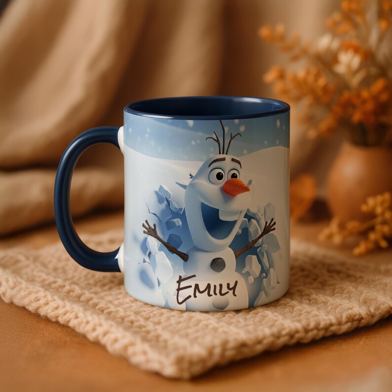 May include: A white ceramic mug featuring a smiling Olaf the snowman from Frozen, with a blue interior and handle. The mug has the name "Emily" printed on it. The background shows a snowy landscape.