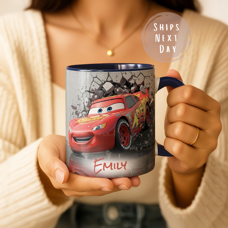 May include: A ceramic mug featuring Lightning McQueen from the Cars movie. The red car is depicted breaking through a gray wall. The mug has a navy blue interior and handle, with the name "Emily" printed on the front.