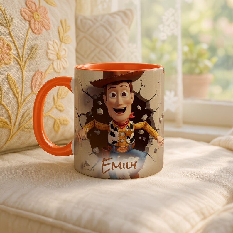 May include: A ceramic mug with a cartoon cowboy design, breaking through a wall. The mug has an orange handle and interior, with the name "Emily" printed on the front. The background includes a window and a decorative pillow.