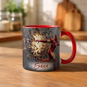 May include: A red and white ceramic mug featuring Iron Man breaking through a wall. The interior and handle are red. The mug has the name "Emily" written on it.