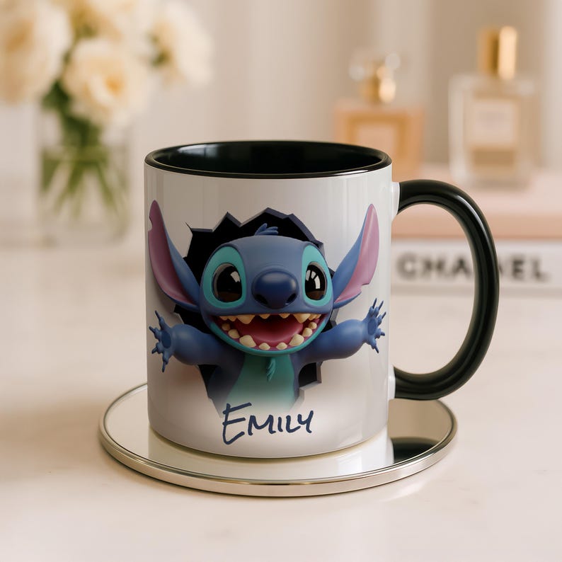 Puede incluir: Taza de cer&aacute;mica blanca con un personaje de dibujos animados azul, con orejas grandes y una amplia sonrisa, saliendo de un agujero dentado. La taza tiene un asa e interior negros, y el nombre "Emily" est&aacute; escrito debajo.