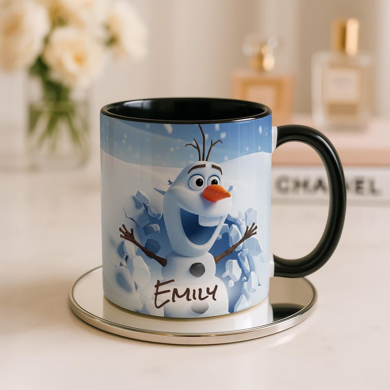 May include: A ceramic mug featuring a cartoon snowman character with a carrot nose and stick arms, set against a snowy background. The mug has a black handle and rim, and the name "Emily" is written on the front.