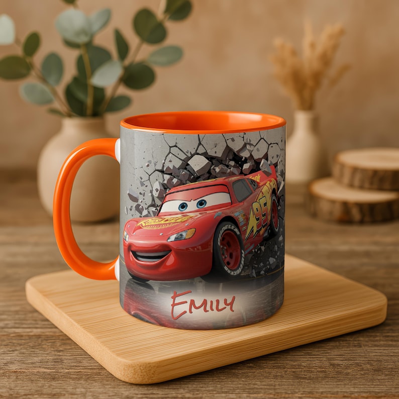 May include: A ceramic mug featuring Lightning McQueen from the Cars movie. The mug has an orange handle and interior, with a design of the red race car bursting through a wall. The name "EMILY" is written on the mug.