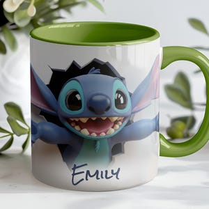 Puede incluir: Taza de cer&aacute;mica blanca con asa e interior verdes. La taza presenta un personaje de dibujos animados rompiendo una pared, con el nombre "Emily" escrito debajo. El personaje es azul con ojos grandes y una amplia sonrisa.