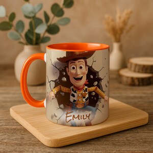 May include: A white ceramic mug with an orange interior and handle. The mug features a colourful image of a cartoon cowboy character breaking through a wall, with the name "EMILY" written below. The mug is on a wooden tray.