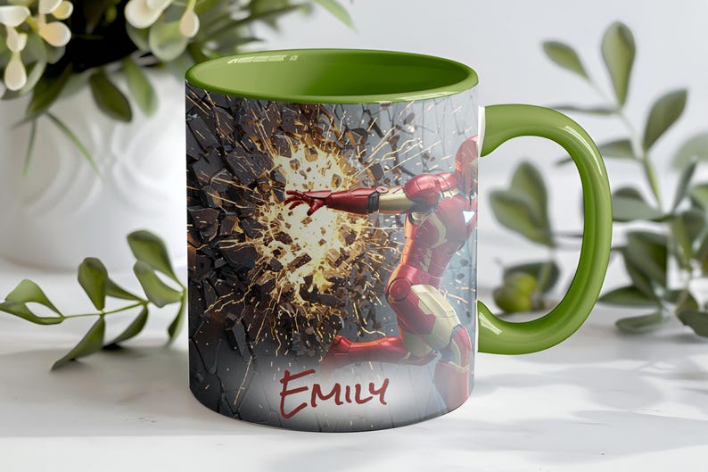 May include: A ceramic mug with a green interior and handle, featuring an illustration of Iron Man breaking through a wall. The design includes the name "Emily" in red script. The mug is white with a wraparound design.