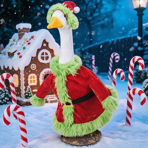 May include: A white goose figurine wearing a red velvet coat with green faux fur trim and a matching red and green hat. The goose has an orange beak and stands on a brown base, positioned in a snowy outdoor setting with candy cane decorations.