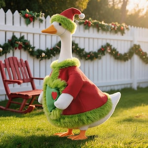 May include: A white plush goose wearing a red coat with green faux fur trim and a matching red hat with a green fur brim. The coat features a green heart-shaped pocket with a small red heart in the center. The goose has an orange beak and feet.