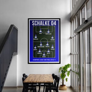Puede incluir: Un póster enmarcado que muestra la alineación de un equipo de fútbol, con el texto "SCHALKE 04" en la parte superior. El póster tiene un borde azul y muestra la formación del equipo en un campo verde. El texto "CHAMPIONS LEAGUE SEMI FINALS 2010/11" está en la parte inferior.