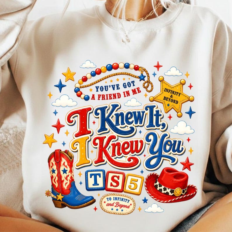 K&ouml;nnte beinhalten: Ein cremefarbenes Sweatshirt mit Rundhalsausschnitt und einem bunten Grafikdruck, der einen Cowboystiefel, einen roten Hut, einen Sheriffstern und Alphabet-Bl&ouml;cke mit der Aufschrift TS5 zeigt. Der Text lautet You've Got A Friend In Me, I Knew It, I Knew You und To Infinity And Beyond.