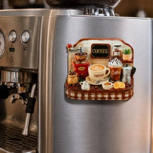 Puede incluir: Un imán decorativo para refrigerador con una escena de cafetería en tres dimensiones. El diseño incluye un molinillo de café rojo, una taza blanca con arte latte etiquetada COFFEE, un café helado, una cafetera moka y un letrero que dice COFFEE.