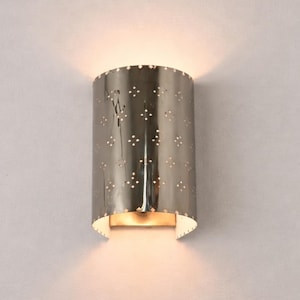 May include: A semi-cylindrical wall sconce with a polished metallic finish. The surface features a repeating pattern of small, diamond-shaped cutouts that allow light to pass through, casting a warm glow above and below the fixture.