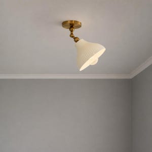 May include: A ceiling-mounted light fixture with a brass finish and a white, ribbed glass shade. The shade is cone-shaped and angled downward, providing focused illumination. The fixture is designed for indoor use.