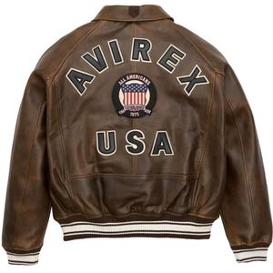 May include: Brown leather bomber jacket with the word "AVIREX" arched across the back, above a patch with the American flag and the words "ALL AMERICANS ESTABLISHED 1975". The word "USA" is below the patch. The jacket has white and black striped cuffs and hem.