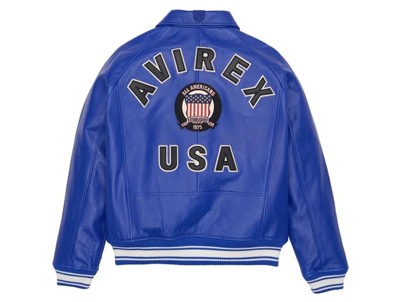May include: A vibrant blue leather jacket with the word "AVIREX" arched across the shoulders in black and white lettering. The back of the jacket features a patch with the American flag and the words "ALL AMERICANS" and "USA". The jacket has white and blue striped cuffs.