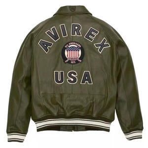 May include: Olive green leather jacket with the word "AVIREX" arched across the back, above a patch with the American flag and the words "ALL AMERICANS ESTABLISHED 1975". The word "USA" is below the patch. The jacket has white and black striped cuffs and hem.