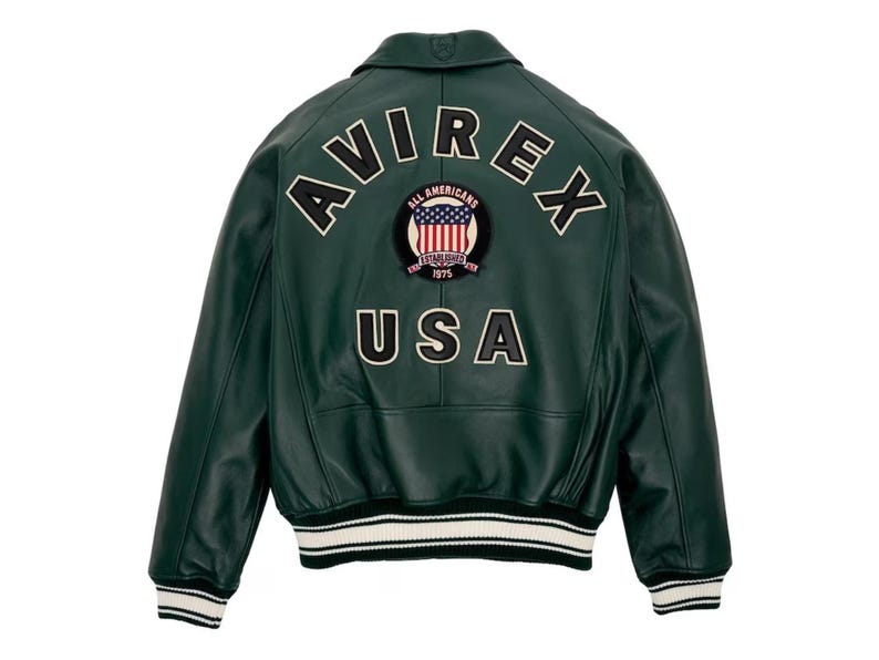 May include: A dark green leather jacket with the text "AVIREX" arched across the upper back, and "USA" below. A patch featuring the American flag is centered between the text. The jacket has a white and black striped hem and cuffs.