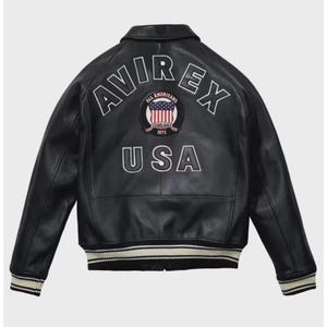 May include: Black leather jacket with the text "AVIREX USA" on the back. The jacket features a white and red emblem with the words "All Americans Established 1975". The jacket has a ribbed collar, cuffs, and hem with white and black stripes.