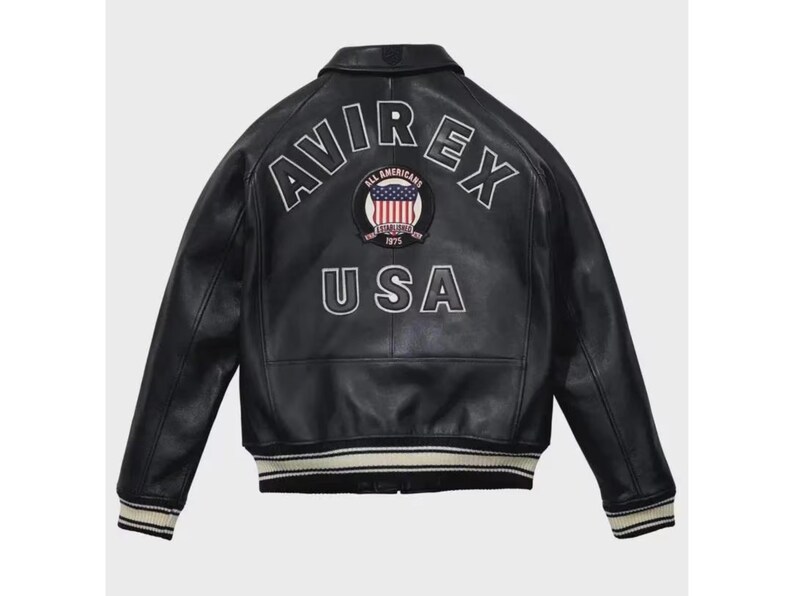 May include: Black leather jacket with the text "AVIREX USA" on the back. The jacket features a white and red emblem with the words "All Americans Established 1975". The jacket has a ribbed collar, cuffs, and hem with white and black stripes.