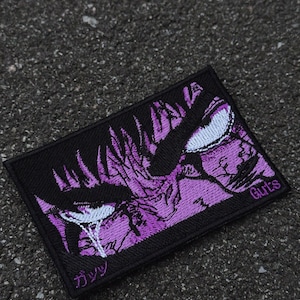 May include: A rectangular black patch featuring a purple illustration of a character's face with white eyes. The word "Guts" is printed in white on the right side, and Japanese characters are on the bottom left.