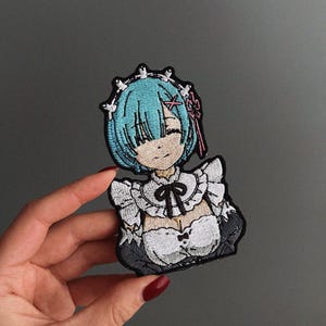 May include: Embroidered patch depicting an anime character with blue hair, a white maid outfit, and a black bow. The patch is intricately designed and features multiple colours, suitable for clothing or accessories.