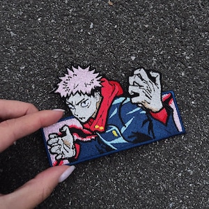 Könnte beinhalten: Gestickter Aufnäher mit einer Figur mit pinkfarbenen, stacheligen Haaren, die eine rote Kapuzenjacke und eine blaue Jacke trägt. Der Aufnäher hat eine rechteckige Form mit blauem Rand, für Kleidung oder Accessoires.
