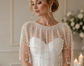 May include: A white pearl beaded capelet featuring multiple draped strands of small round pearls and teardrop-shaped pearl accents. The accessory covers the shoulders and upper chest, creating a layered fringe effect over a plain white garment.