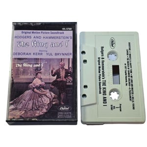May include: A vintage cassette tape of the "The King and I" original motion picture soundtrack. The cassette case features a photo of Deborah Kerr and Yul Brynner. The tape is off-white with the tracklist printed on it.