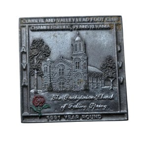 Op de afbeelding: Een rechthoekige, zilverkleurige metalen plaat met een gedetailleerd reliëf van een kerk, bomen en een roos. De tekst "CUMBERLAND VALLEY LEAD FOOT CLUB CHAMBERSBURG, PENNSYLVANIA" en "The Presbyterian Church of Falling Spring 1991 YEAR ROUND" zijn gegraveerd.