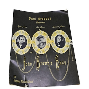 May include: A vintage black theatre programme for "John Brown's Body" by Stephen Vincent Benet. The cover features portraits of Tyrone Power, Anne Baxter, and Raymond Massey in gold frames, with gold text and chain accents.
