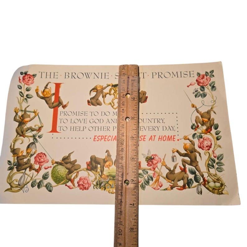 May include: Vintage print featuring whimsical illustrations of brown gnomes and pink roses. The print includes text that reads "THE BROWNIE ST-PROMISE" and other text. A wooden ruler is placed vertically on the print, measuring approximately 8 inches.