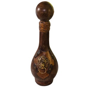 Peut inclure: Une bouteille décorative en cuir marron avec un bouchon rond en bois. La bouteille présente une tête de lion en laiton avec un anneau et est ornée d'accents en cuir. Une pièce unique pour la décoration intérieure ou un bar.
