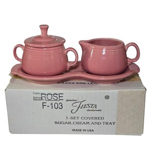 Könnte beinhalten: Ein rosafarbenes Fiesta-Geschirrset mit einem Zuckertopf mit Deckel, einem Sahnekännchen und einem Tablett. Das Set in der Farbe Rose, Muster F-103, wird in einer Box mit der Aufschrift "1-SET COVERED SUGAR, CREAM AND TRAY" und "MADE IN USA" geliefert.