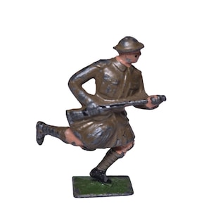 May include: A vintage toy soldier figurine in a running pose, holding a rifle. The soldier is dressed in a khaki uniform and helmet, with a green base. The figurine shows signs of wear, suggesting it is an antique.