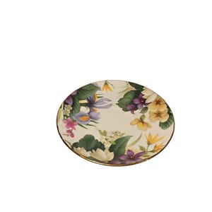 Può includere: Un piattino in ceramica bianca con un bordo dorato presenta un disegno floreale con fiori viola, gialli e bianchi su uno sfondo di foglie verdi.