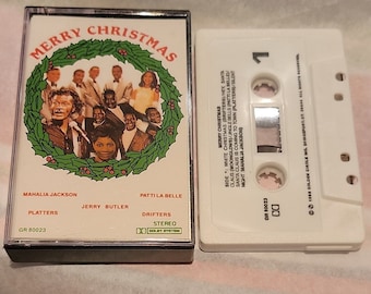 Op de afbeelding: Een witte cassetteband met een zwart label. Het label heeft een groene hulstkrans met een groep zangers erin. De tekst "Merry Christmas" is in rode letters boven de krans gedrukt. De cassetteband is gelabeld met de namen van de zangers, waaronder Mahalia Jackson, Jerry Butler, Patti La Belle en The Platters. De cassetteband is gelabeld met de titel "Merry Christmas" en het catalogusnummer "GR 80023".
