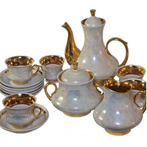 May include: A white porcelain tea set with gold accents. The set includes a teapot, creamer, sugar bowl, and six cups and saucers. The porcelain has an iridescent finish.