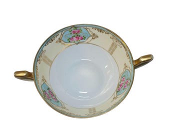 May include: A white porcelain soup bowl with gold trim and floral designs in pink, blue, and green. The bowl has two handles.