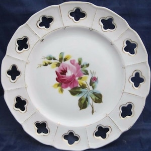 May include: White porcelain plate with a gold rim and openwork design. The plate features a hand-painted pink rose with green leaves.