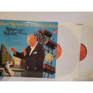 May include: A vintage vinyl record cover featuring a conductor in a tuxedo, a Ferris wheel, and the text "Zwei Herzen im Dreivierteltakt Robert Stolz dirigiert seine Welterfolge".