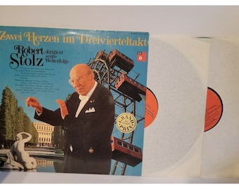 May include: A vintage vinyl record cover featuring a conductor in a tuxedo, a Ferris wheel, and the text "Zwei Herzen im Dreivierteltakt Robert Stolz dirigiert seine Welterfolge".