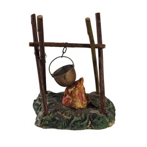 May include: A miniature campfire scene with a small metal pot hanging over a painted flame. The scene includes wooden poles and a base with green and brown details, creating a rustic aesthetic.