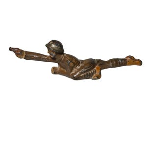 May include: A vintage toy soldier, cast in bronze-coloured metal, in a prone firing position. The soldier is depicted wearing a helmet and uniform, with a rifle extended. The toy has an aged patina.