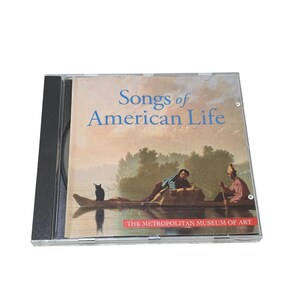 May include: A CD case featuring the title "Songs of American Life" in blue lettering. The cover art is a painting of people in a boat on a river. The Metropolitan Museum of Art logo is at the bottom.