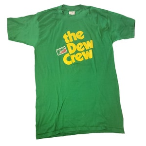 May include: Green t-shirt with a yellow and red Mountain Dew logo and the text "the Dew Crew" in yellow.