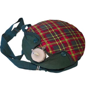May include: A vintage canteen with a plaid pattern in red, yellow, and black. The canteen has a green fabric base and strap, with a metal clasp and a small, round, light-colored stopper. The canteen is designed to be worn over the shoulder.