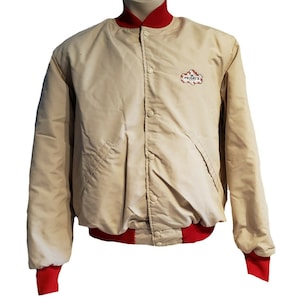 May include: A beige bomber jacket with red ribbed trim and a T.G.I. Friday's logo patch on the left chest.