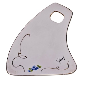 Può includere: Piatto da portata in ceramica bianca dalla forma unica con foro per la maniglia. Presenta un bordo dorato, decorazioni floreali blu e una firma. Ideale per servire antipasti o piccoli piatti.