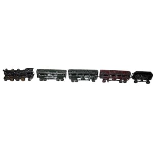 May include: A vintage toy train set comprising a black locomotive, two green carriages, a red carriage, and a black coal truck. The train cars are lined up, displaying their detailed design and aged appearance.