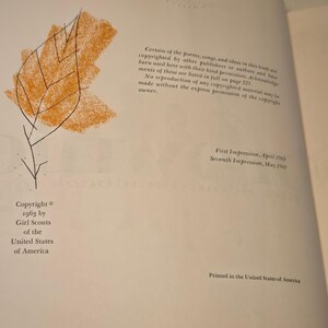 May include: An open book page with text and an illustration of a leaf. The leaf is orange with black veins, and the text includes copyright information from 1963 by Girl Scouts of the United States of America.